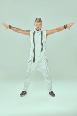 Mohawk ve dövmeleri olan yakışıklı havalı bir punk rock müzisyeni hafif bir stüdyonun arka planında kollarını yana açmış şekilde poz veriyor. Siber punk stili. 