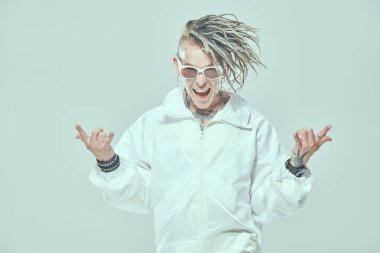 Rastalı ve güneş gözlüklü şık bir punk rock müzisyeni beyaz takım elbise içinde bağırıyor ve güzel jestler yapıyor. Gençlik alternatif kültürü. Beyaz stüdyo geçmişi. 
