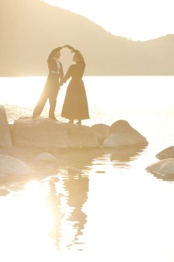 Şık giyimli çift gün batımında denizin kenarında el ele tutuşup birbirlerinin gözlerine bakıyor. Tarihi aşk romanı. Sevgi dolu bir ilişki. 19. yüzyıl tarzı.