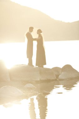 Zarif siyah elbiseli güzel romantik çift gün batımında deniz kenarındaki perdenin altında düşünceli bir şekilde dururlar. Aşk, ilişki. Aşk romanı. Gizli aşk. 19. yüzyıl tarzı.