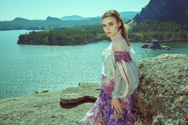 Güzel kız model şık etnik kıyafetlerle poz veriyor, güzel bir gölün arkasındaki bir dağın tepesinde duruyor. Moda ve etnik tarz. Seyahat ve tatil. 