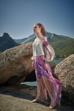 Güzel kız model şık etnik giysiler içinde, bir dağın tepesinde rüzgara karşı duruyor. Moda ve etnik tarz.