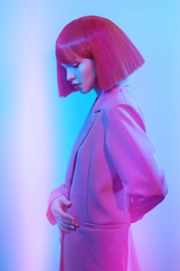 Parlak makyajlı, parlak kırmızı saçlı, şık pembe ceketli, karışık renk ışıklandırmalı güzel bir kız modelin yan görüntüsü. Saç stili, saç boyası, makyaj. Moda ve parlak renkler. 