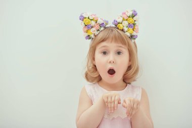 Pembe yaz elbisesi ve çiçekli, ağzı açık ve elleri sıkıca önünde duran dört yaşında güzel bir kızın portresi. Çocuk modası. Boşluğu kopyala.