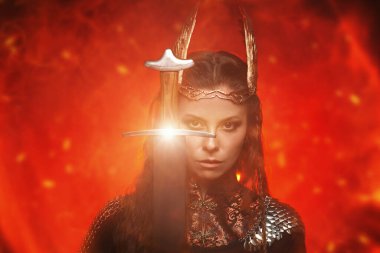 İskandinav mitolojisi. Kanatlı kasklı güzel bir Valkyrie, yanan ateşin arka planında önlerinde bir kılıç tutuyor.. 