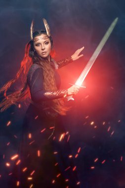 Kutsal kadın savaşçı Valkyrie 'nin portresi elinde bir kılıçla savaşıyor. Efsanevi fantezi. İskandinav mitolojisi. Dumanlı koyu arkaplan, ateş kıvılcımları ve kırmızı ışık.