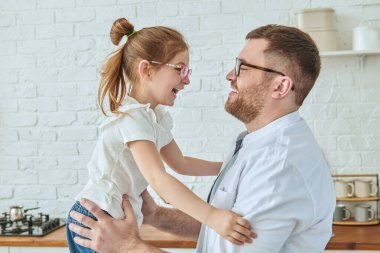 Mutlu baba ve küçük kızın portresi gülüyor ve modern bir mutfakta neşeyle vakit geçiriyor. Modern iç mekan, mutfak mobilyası. Mutlu aile. 