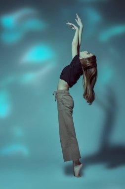 Çağdaş bale. Modern balerin, gri arka planda ışıklarla zarif bir şekilde dans eder. Dans ifadesi. Tam boy portre.