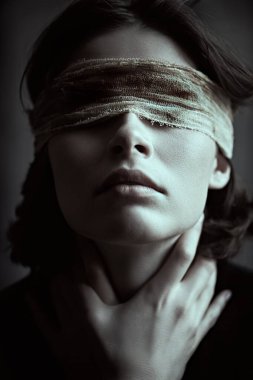 Koyu renk saçlı, sargılı gözlü bir kız elleri ile boynunu tutarak karanlık bir yerde duruyor, acı çekiyor ve kendi içine çekiliyor. İnsanların acıları, körlükleri. 