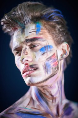 Sanat ve erkek güzelliği. Siyah arka planda renkli yüzü olan yakışıklı bir adamın portresi. Sanat ve moda. Vücut boyası.
