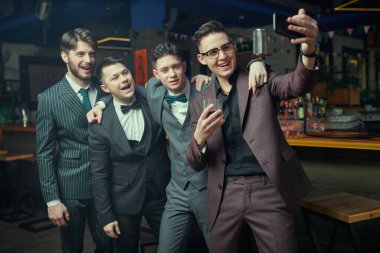 Zarif, klasik takım elbiseli bir grup yakışıklı genç bir barda rahatlar ve selfie çekerler. Erkek modası. İş adamları kulübü.