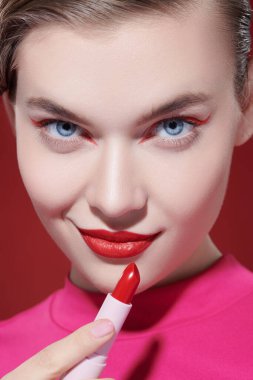 Güzellik kızı. Sevimli kırmızı renk. Parlak makyajlı, gülümseyen ve elinde muhteşem kırmızı ruj olan güzel bir kız modelin portresi. Yakın çekim..