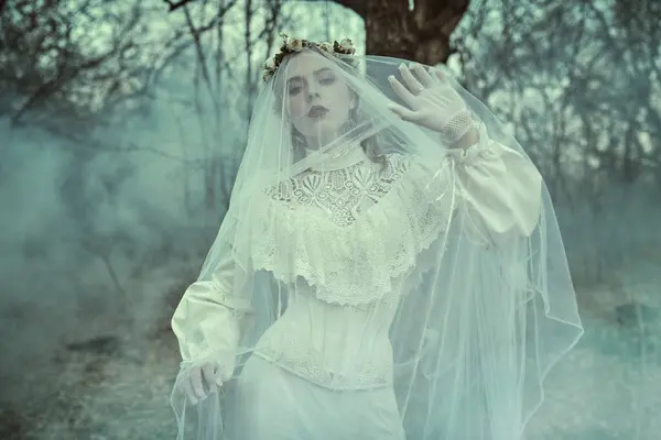 Stock image Mystical love novel. Portrait of a beautiful bride lady in a white dress and covered with a veil, wandering alone through the old park. Ghost of bride. Victorian style. 