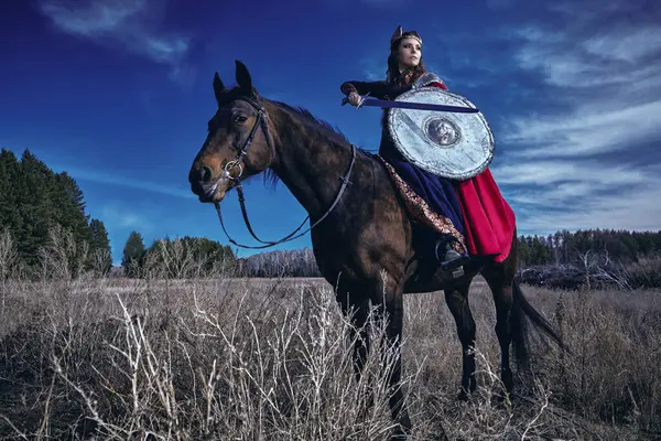 Cesur ve güzel kadın savaşçı Valkyrie elinde bir kılıç ve kalkanla savaş atının üzerinde oturuyor. İskandinav mitolojisi. Efsanevi fantezi.