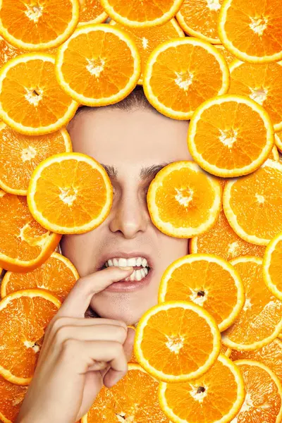 stock image Close-up portrait of an emotional young male chef, laid by oranges, holding his finger in his mouth. Fresh fruits and juices. Vitamins.