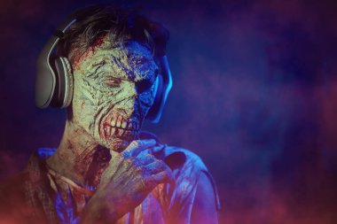 Vahşi bir zombi adam kulaklıkla müzik dinler ve düşünceli bir şekilde ileriye bakar. Karanlık bir arka plan ve gizemli bir sis. Uzayı kopyala Rock müziği. Kıyametten sonraki hayat. Cadılar Bayramı, korku.