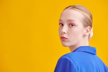 Moda ve güzellik. Sarı stüdyo arka planında mavi takım elbiseli, yumuşak pembe makyajlı güzel sarışın bir kızın portresi. Uzayı kopyala Parlak yaz renkleri.