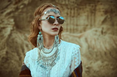 Boho tarzı, yaz tarzı. Zarif bir boho tarzı mücevher ve gözlüklü güzel bir kadın çöldeki kum tepelerinin arkasında duruyor..