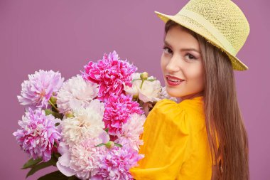 Yazlık kıyafetleri ve şapkasıyla gülümseyen güzel bir kız bir buket yumuşak yaz çiçeğiyle poz veriyor. Yaz modası. Güzellik ve çiçekler, makyaj.