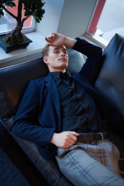 Yakışıklı, iyi giyimli genç bir adam kanepede dinleniyor ve hafifçe gülümsüyor..