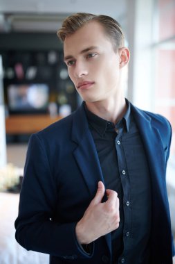 Modern bir ofiste duran şık takım elbiseli genç ve yakışıklı bir işadamının portresi. Ofis ve ev için iç mekan.