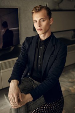 Akıllı takım elbiseli ciddi bir genç işadamı modern dairesinde oturmuş kameraya bakıyor. İş konsepti. 