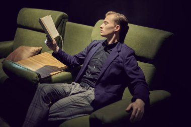 Ofisinde kanepede oturup kitap okuyan genç ve yakışıklı bir işadamının portresi. Ofis ve ev için mobilya ve iç dekorasyon.