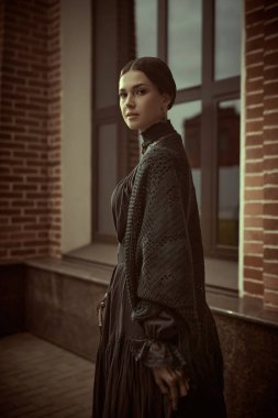 Katı siyah elbiseli, siyah saçlı, sırtı kıllı, caddede duran hoş, sofistike bir bayan. 19. yüzyılın romanının kahramanı..