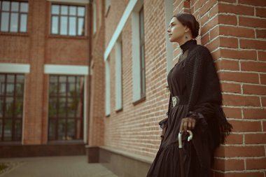 Katı siyah elbiseli, sırtı siyah saçları çekilmiş, sokakta duvara yaslanmış hoş, sofistike bir bayan. 19. yüzyılın romanının kahramanı. Boşluğu kopyala.