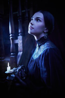 The heroine of the novel of the 19th century. A beautiful aristocratic girl in a black dress stands by the staircase in a night house with a candle in her hand. Mystical atmosphere.  clipart