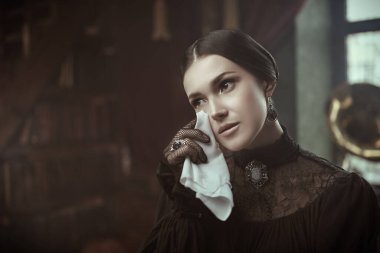 A beautiful sad girl of noble origin stands in a rich room in a mourning black dress and wipes her tears. The heroine of the 19th century novel, a dramatic story. clipart