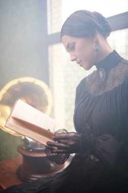 Romanın 19. yüzyıl kahramanı. Siyah, sıkı elbiseli, sırtı kıllı aristokrat bir kadın pahalı dekorasyonlarla dolu bir odada oturmuş kitap okuyor..