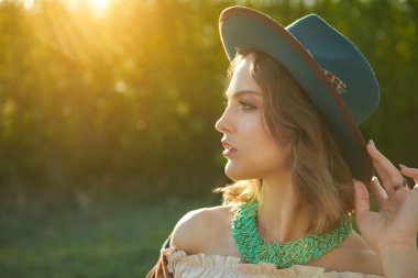 Boho tarzı kıyafetler ve aksesuar giymiş muhteşem bir kızın portresi batan güneşin sıcak ışınlarında kırsalda. Yaz tatili. Bohem, modern hippi tarzı. Boşluğu kopyala.