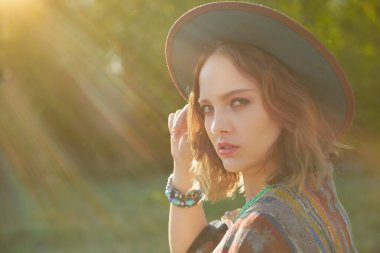 Boho tarzı kıyafetler ve aksesuar giymiş muhteşem bir kızın portresi batan güneşin sıcak ışınlarında kırsalda. Yaz tatili. Bohem, modern hippi tarzı.. 