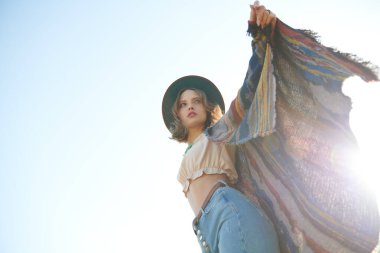 Parlak güneş ışığı altında mavi bir gökyüzünün arka planında poz veren Boho tarzı bluzlu güzel bir kız. Bohem, modern hippi tarzı. Yaz modası. Tatil ve seyahat. Boşluğu kopyala.