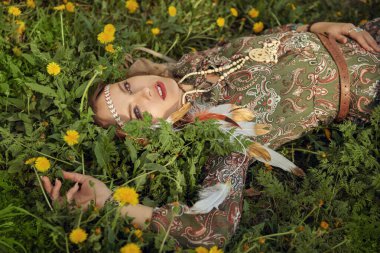 Bahar sezonu. Yeşil çimlerin üzerinde karahindibaların arasında yatan güzel ve narin bir kızın portresi. Romantik tarzda. Güzellik ve moda, bohem ve hippi tarzı. 