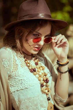 A gorgeous girl model poses in boho style clothes and accessories on a sunny summer day outdoors. Fashion shot. Boho and hippie style. clipart