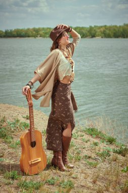 Boho tarzı kıyafetleri ve mücevherleri olan güzel bir kızın portresi nehir kıyısında sevinçle duruyor ve uzaklığa bakıyor. Yaz tarzı, moda. Hippi kız. Tatil, seyahat. 