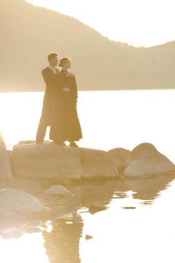 Siyah 19. yüzyıl tarzında giyinmiş romantik çift gün batımında deniz kenarında birbirlerine yakın dururlar ve duygularından acı çekerler. Aşk, ilişki. Tarihi roman, drama..
