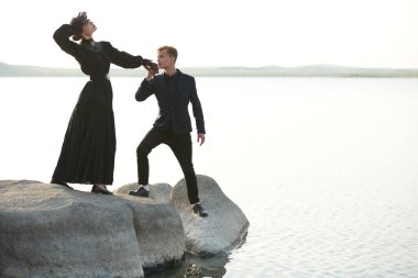 Genç yakışıklı bir adam, gün batımında sahilde duran genç ve güzel bir kadının elini öpüyor. Tarihi aşk romanı. Sevgi dolu bir ilişki. 19. yüzyıl tarzı.