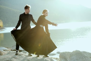 Gün batımında denizin kenarında duran siyah şık elbiseli romantik çiftin portresi. Tarihi aşk romanı. 19. yüzyıl.