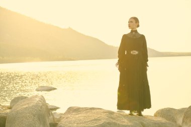 Siyah bir elbise içinde güzel, zarif bir kadın denizin kenarında dikiliyor. Düşünceli ve gergin bir şekilde uzaklığa bakıyor sanki birini bekliyor gibi. 19. yüzyıl romanı. Boşluğu kopyala.