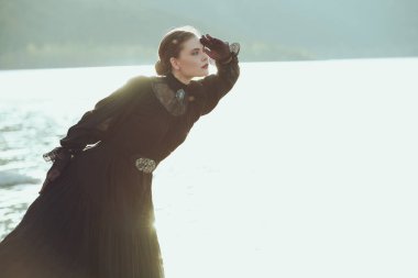 Siyah bir elbise içinde güzel, zarif bir kadın denizin kenarında dikiliyor sanki birini bekliyormuş gibi dikkatlice uzaklara bakıyor. 19. yüzyıl romanı. 