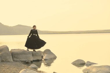 19. yüzyıl romanı. Siyah bir elbise giymiş güzel genç bir kadın denizin kenarında duruyor ve sanki birini bekliyormuş gibi uzaktan bakıyor. Boşluğu kopyala.