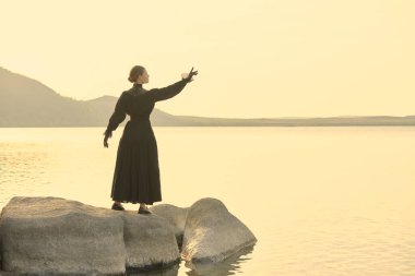 Siyah bir elbise içinde güzel, zarif bir kadın denizin kenarında dikiliyor. Düşünceli ve gergin bir şekilde uzaklığa bakıyor sanki birini bekliyor gibi. 19. yüzyıl romanı. Boşluğu kopyala.