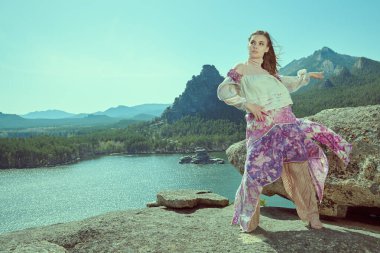 Güzel kız model şık etnik giysiler içinde, rüzgarla savrulan bir dağda duruyor. Moda ve etnik tarz. Boşluğu kopyala.