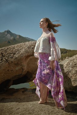 Güzel kız model şık etnik giysiler içinde, bir dağın tepesinde rüzgara karşı duruyor. Moda ve etnik tarz.