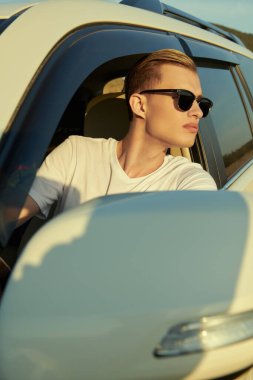 Yakışıklı genç bir adam arabasının direksiyonunda oturur ve tatildeyken pencereden dışarı bakar. Tatil, yaz tatili ve seyahat. Araba yolculuğu..