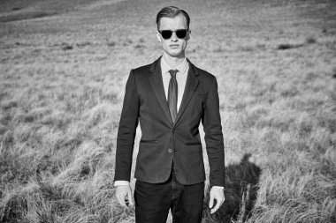 Siyah klasik takım elbiseli ve siyah güneş gözlüklü yakışıklı bir adamın siyah beyaz portresi açık bir alanda duruyor ve kameraya ciddi ciddi bakıyor. Süper insan.