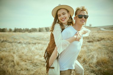 Aşk, yaz, özgürlük. Yakışıklı adam sırtına gülümseyen neşeli bir kız taşıyor. Güzel manzara ve mavi gökyüzü arkaplanı. Sevgi dolu bir çift. Yaz tatili ve seyahat.